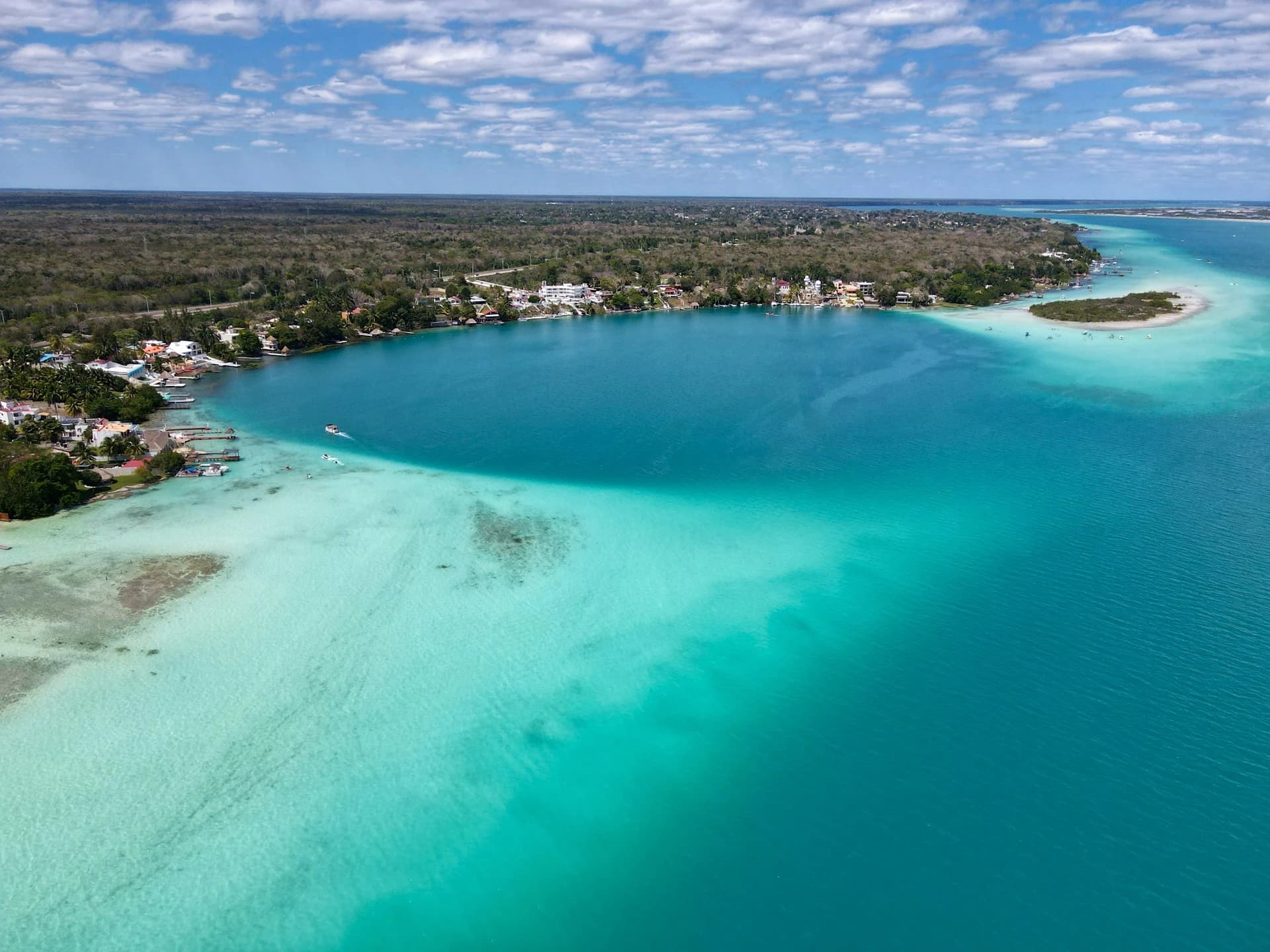 Storm clouds clearing over a calm, empty Bacalar Lagoon with a wooden dock on a September morning