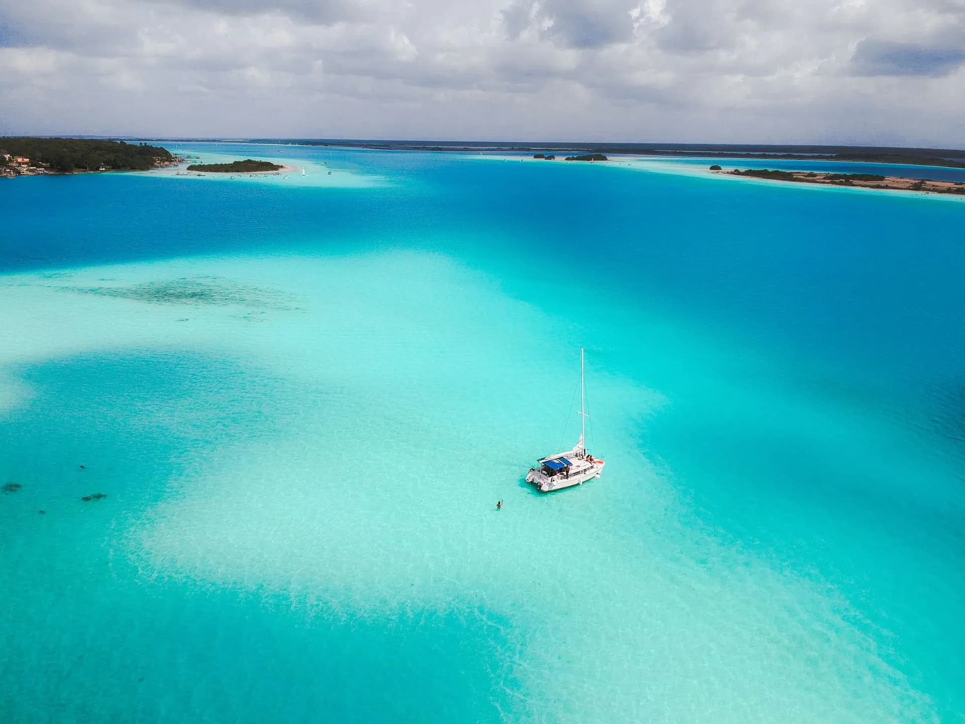 Sailboat gliding across the pale turquoise and deep blue bands of Bacalar Lagoon, Quintana Roo
