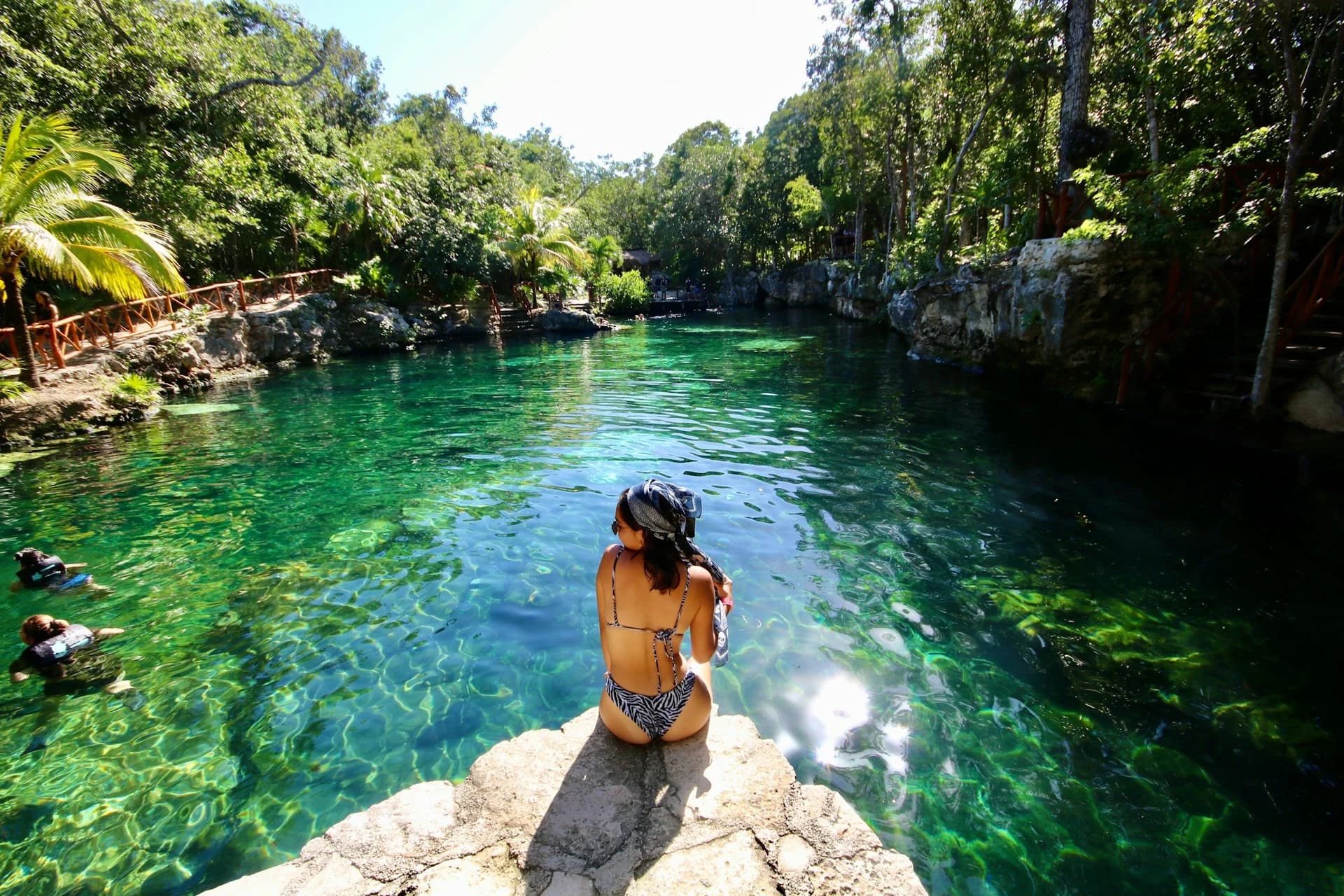 Snorkeler in the clear blue water of a jungle cenote with sunbeams and stalactites near Cancún, Mexico