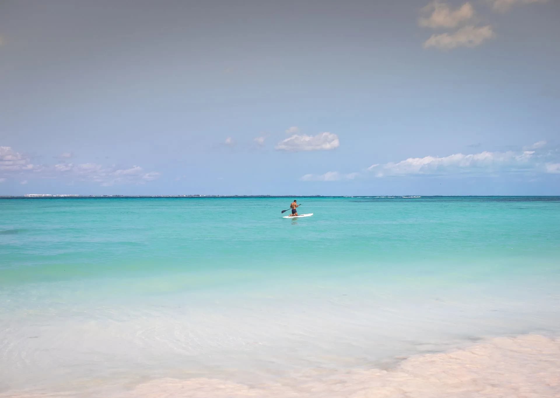 Calm turquoise Caribbean water and a near-empty Hotel Zone beach in Cancún in September with late-summer clouds on the horizon