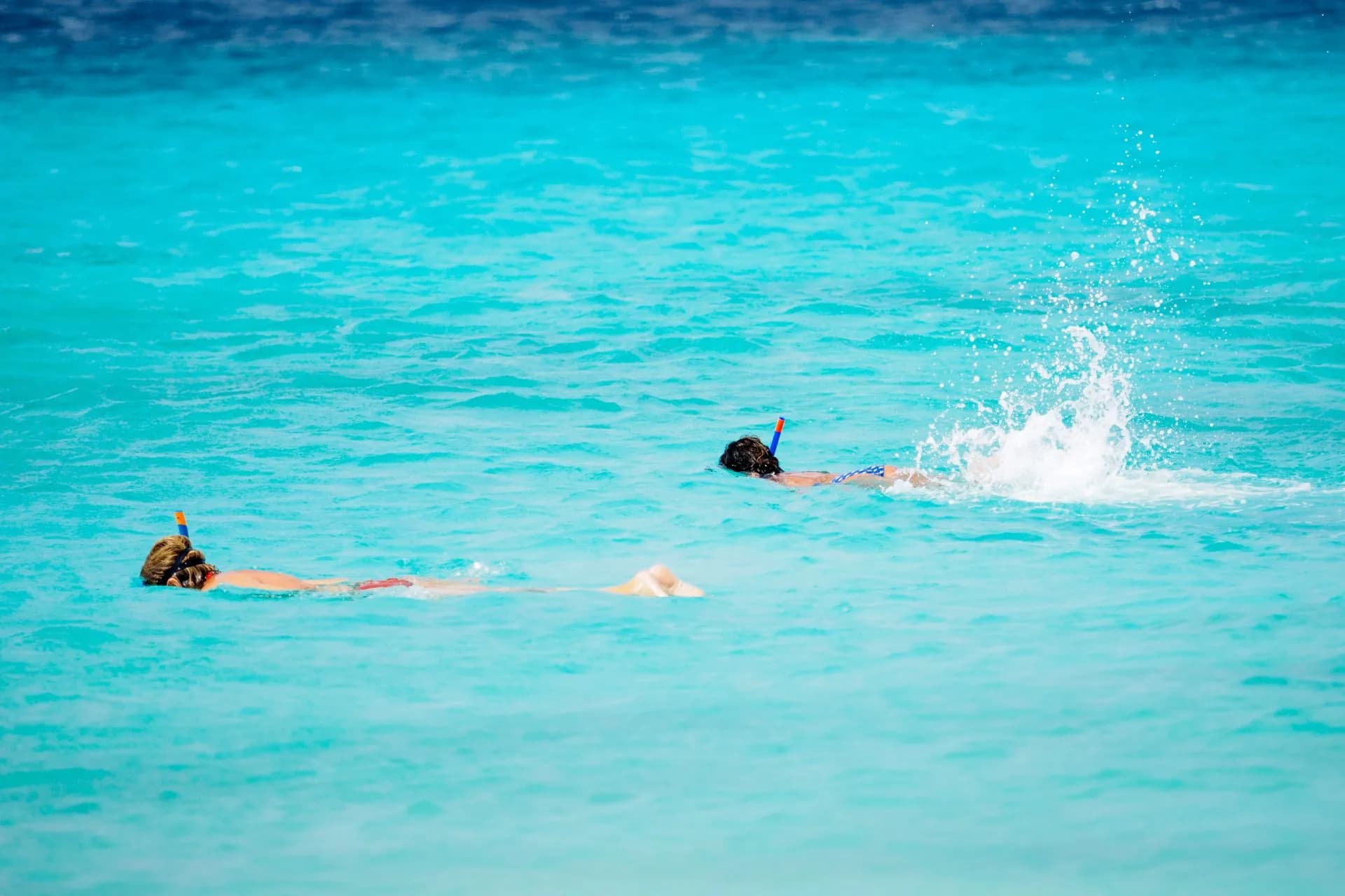 A see-through clear-hull boat over shallow turquoise reef water off Cozumel with snorkelers nearby