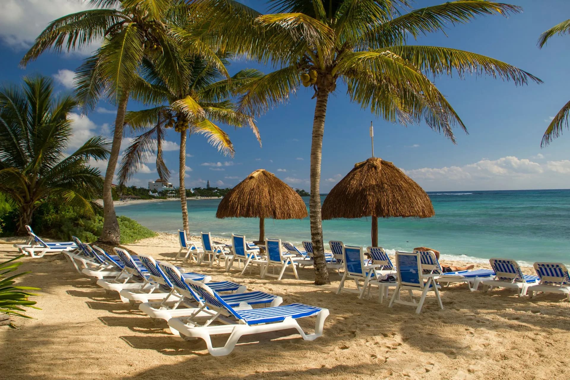 Palm-shaded loungers and calm turquoise Caribbean water at a Cozumel beach club on a sunny day