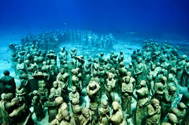 Cientos de estatuas de concreto de tamaño real sobre arena blanca en agua azul profundo, en la galería de Manchones frente a Isla Mujeres