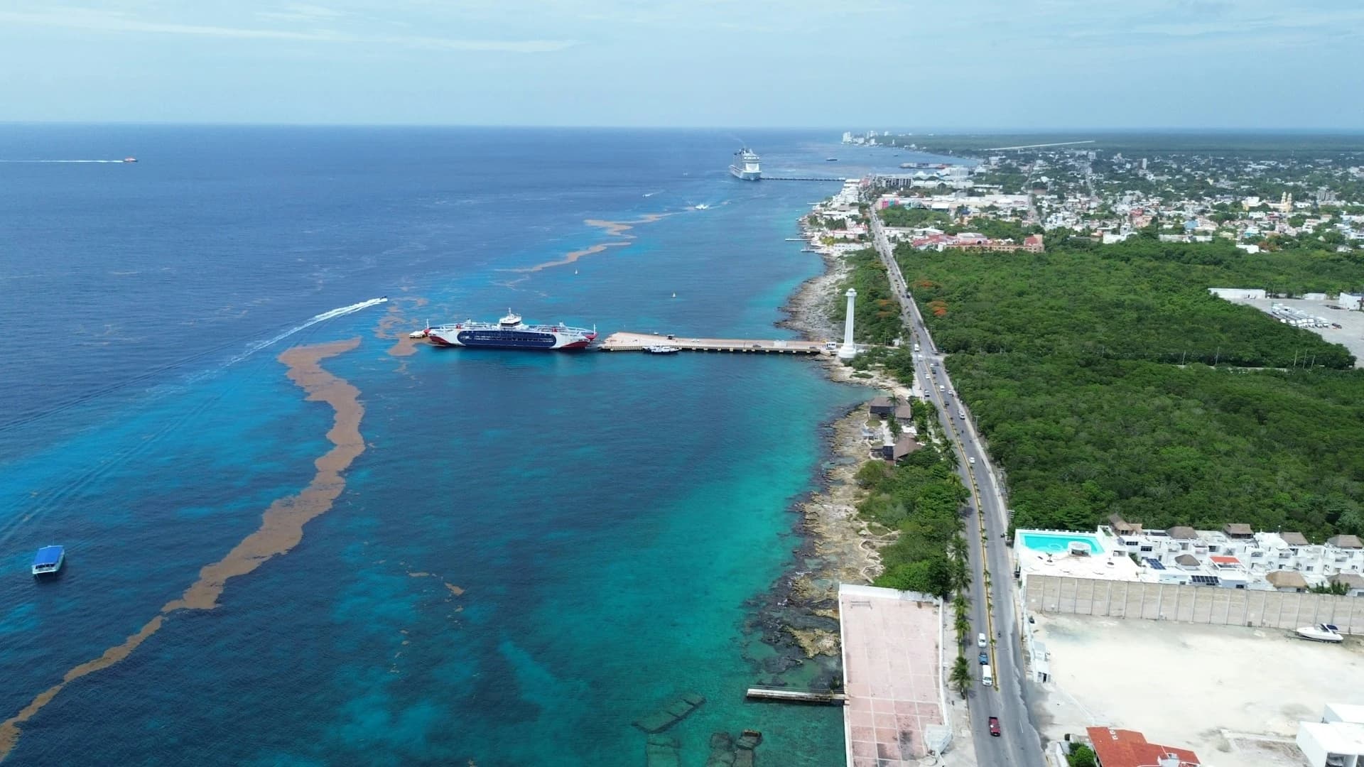 Un ferry blanco de pasajeros saliendo del largo muelle de Playa del Carmen rumbo a Cozumel sobre el agua turquesa del Caribe